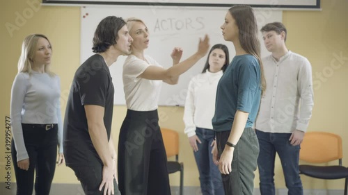 Group of male and female actors studying in auditorium. Professional Caucasian teacher showing slap in face to adult students. Professional acting and studying concept. photo