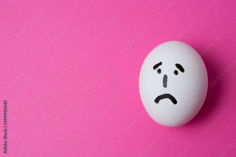 Fototapeta premium An egg with a sad face, on a pink background with copy space.