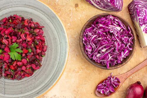 top view beet salad on a plate with red onions and chopped red cabbage in a bowl on a wooden table
