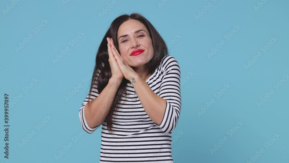 Funny young woman 20s in striped shirt posing isolated on blue background. People lifestyle concept. Sleep with folded hands under cheek waking up waving and greeting with hand as notices someone Funny young woman 20s in striped shirt posing isolated on blue background. People lifestyle concept. Sleep with folded hands under cheek waking up waving and greeting with hand as notices someone