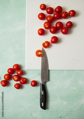 Cherry tomatoes lie on a light pink cutting board next to a knife on a blue background
