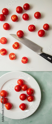 Cherry tomatoes in a white plate lie next to a knife and a light pink board on a blue background
