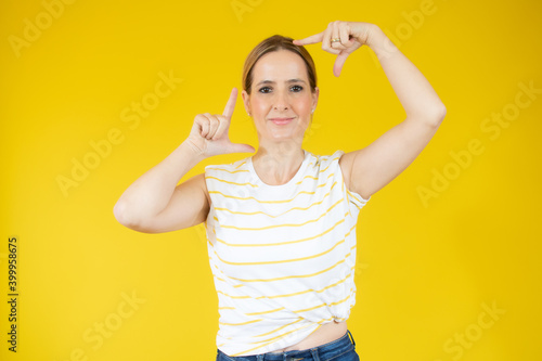 Young blonde woman wearing casual t-shirt smiling making frame with hands and fingers with happy face. creativity and photography concept.