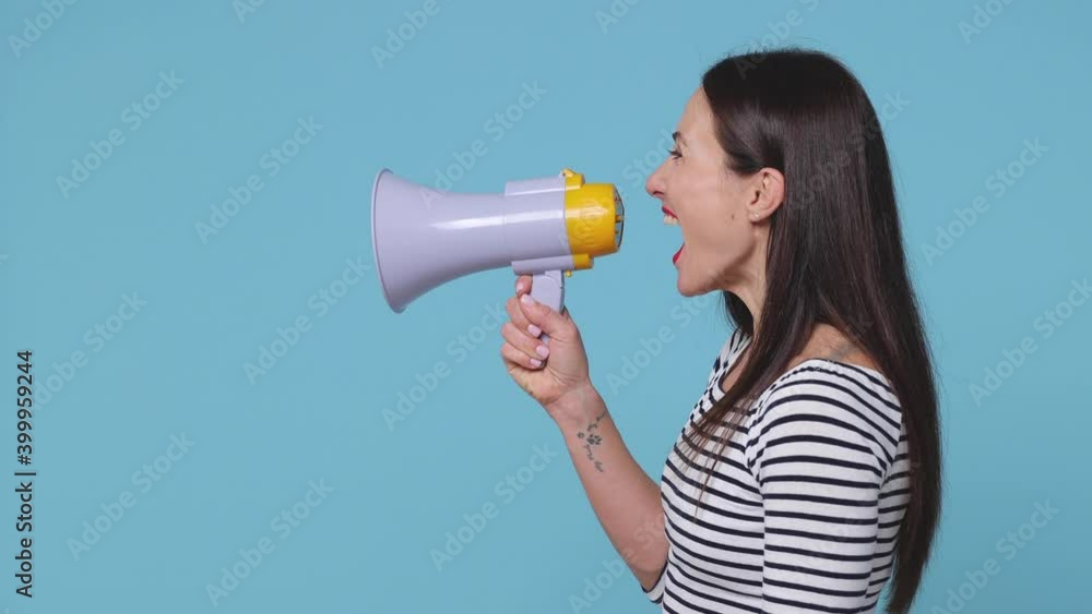 Side profile view of cheerful brunette young woman 20s in striped shirt posing isolated on blue background studio. People lifestyle concept. Looking aside screaming in megaphone turn around camera Side profile view of cheerful brunette young woman 20s in striped shirt posing isolated on blue background studio. People lifestyle concept. Looking aside screaming in megaphone turn around camera