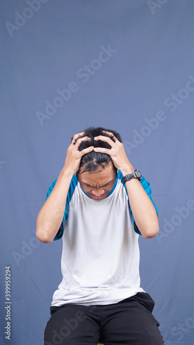 asian man stress gesture and expression holding head and hair with isolated blue background