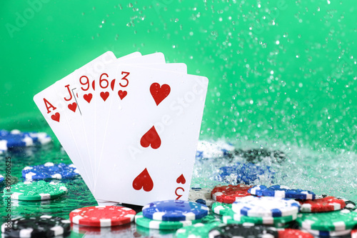 Flush poker combination under the water drops and falling poker chips against green background. Online gambling. Betting. Gambling addiction.