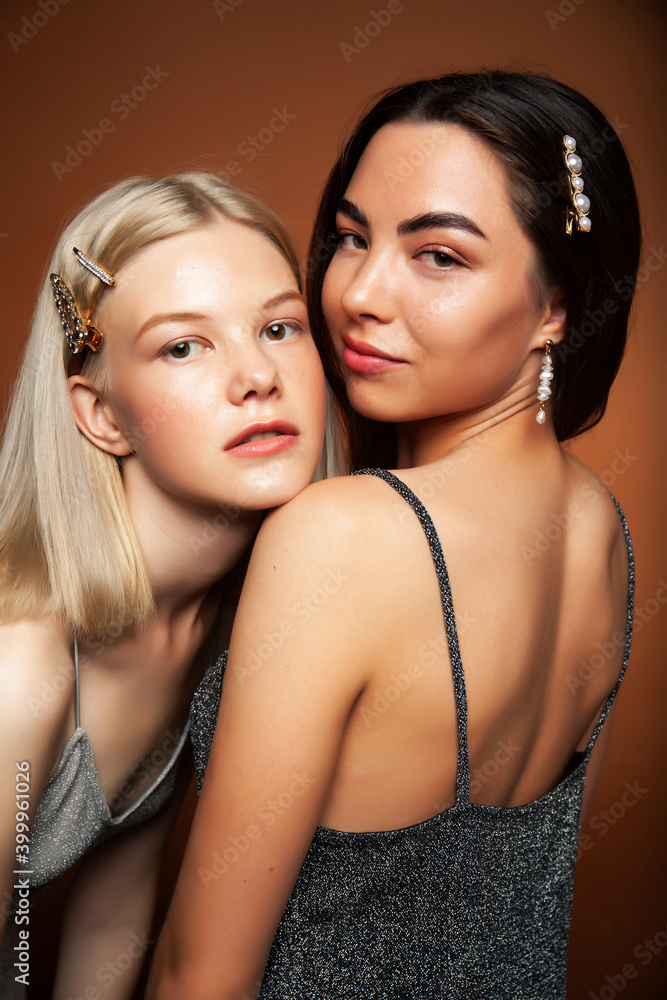 two pretty diverse girls happy posing together: blond and brunette on brown background, lifestyle people concept two pretty diverse girls happy posing together: blond and brunette on brown background, lifestyle people concept