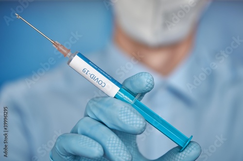 Close up of a researcher with face mask holding a syringe with coronavirus vaccine.