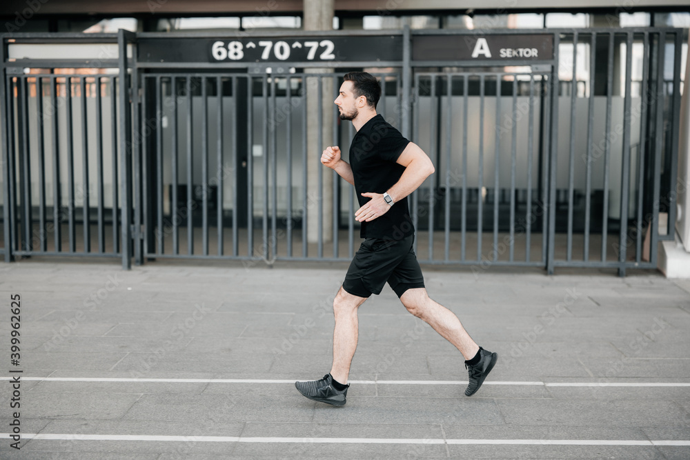 Concentrated male runner excercising at morning. Urban city lifestyle concept. Athletic man in black sport clothes and sneakers jogging outdoors. Healthy lifestyle. Man running. Active living.