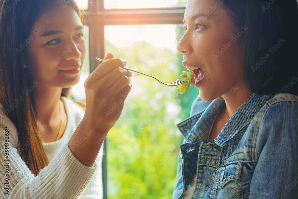 © Panumas - LGBT Lesbian Asian couple romantic moments eating vegetable salad in restaurant.