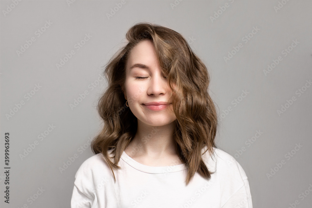 Portrait of happy smiling young woman with closed eyes, gray background, copy space. Beautiful caucasian girl with brown curly hairstyle. Cheerful, satisfied, dreamy expression face. Calmness, relax Portrait of happy smiling young woman with closed eyes, gray background, copy space. Beautiful caucasian girl with brown curly hairstyle. Cheerful, satisfied, dreamy expression face. Calmness, relax