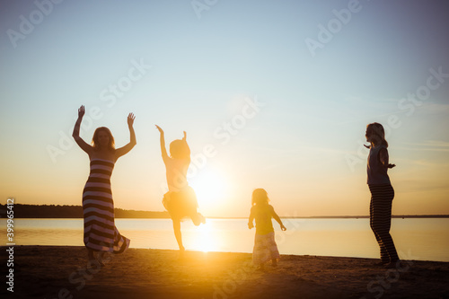 Silhouettes of children and their mothers jumping and having fun on the beach in sunset light. Good mood and pastime among the younger and older generation. Beautiful landscape. Childhood happiness