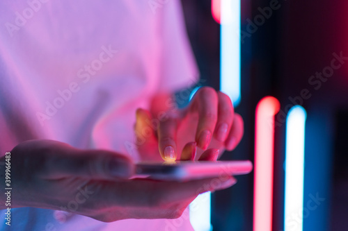 Mobile phone in the light of neon in women's hand. A person writes a message in a chat on the colored background