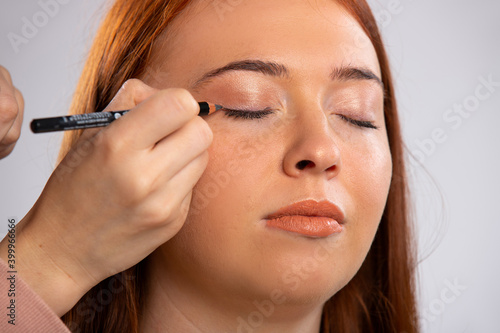 Closeup photo of make up for a red-haired girl, closed eyes and a eyeliner cosmetic pencil. Beauty concept.