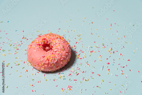 Yummy pink donut with colorful sprinkles on blue background.