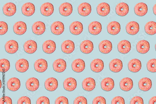 Pattern of a yummy pinks donuts with colorful sprinkles on blue background.