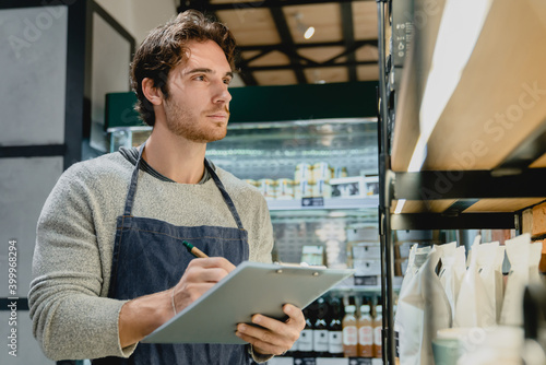 Young handsome caucasian waiter checking the quality of goods holding a folder in cafeteria photo