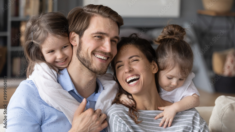 Close up wide banner panoramic view of happy young Caucasian family with two small daughters have fun at home. Smiling mom and dad feel playful enjoy weekend relaxing with little girls children. Close up wide banner panoramic view of happy young Caucasian family with two small daughters have fun at home. Smiling mom and dad feel playful enjoy weekend relaxing with little girls children.