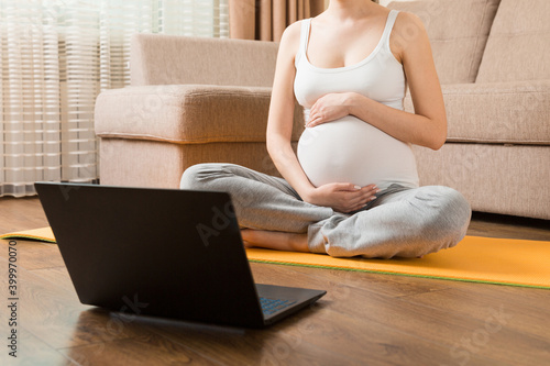 Young happy healthy yoga fitness beautiful pregnant woman doing bakasana yoga workout on yoga mat opposite laptop with online master class. lifestyle concept at coronavirus time