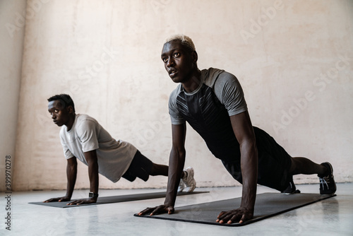 Two young african american men doing workout on exercise mat indoors