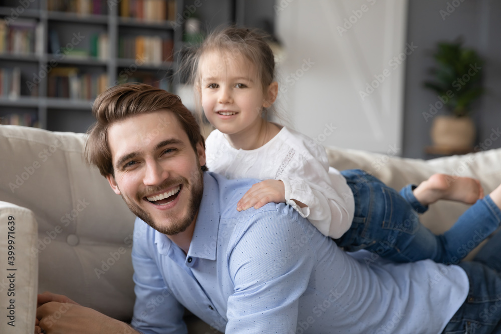 Portrait of happy young Caucasian father lying on couch relaxing playing with small daughter. Smiling dad rest on sofa in living room with excited cute little girl child, enjoy family leisure weekend. Portrait of happy young Caucasian father lying on couch relaxing playing with small daughter. Smiling dad rest on sofa in living room with excited cute little girl child, enjoy family leisure weekend.