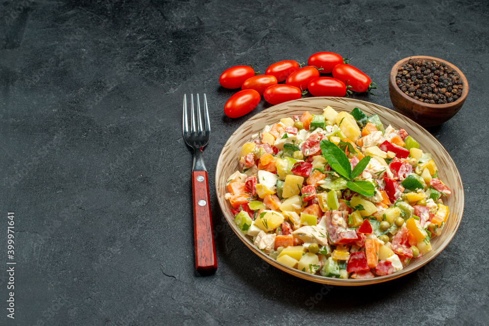 side close view of bowl of veggie salad with fork tomatoes pepper on side and free place for text on dark grey table side close view of bowl of veggie salad with fork tomatoes pepper on side and free place for text on dark grey table