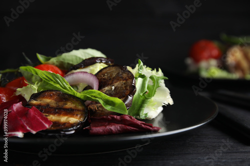 Delicious salad with roasted eggplant and basil served on black wooden table, closeup