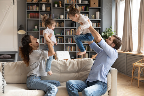 Overjoyed young family with two small daughters feel playful engaged in funny activity on weekend at home. Happy parents mom and dad have fun play together with little girls children in living room.