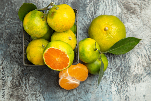 Above view of a basket with fresh green tangerines cut in half and peeled tangerine on gray background