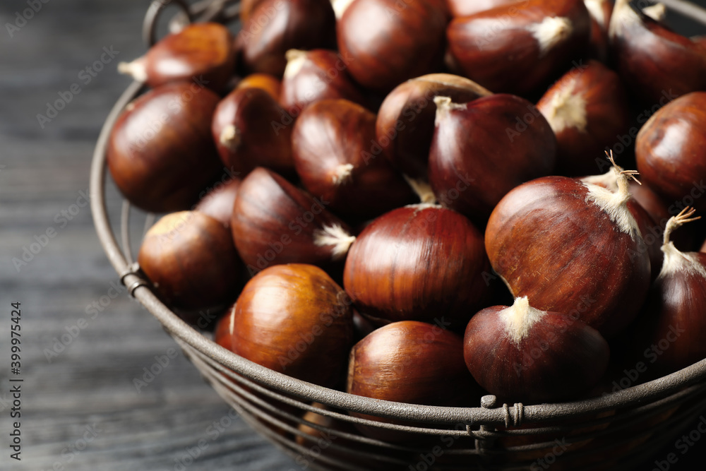 Obraz premium Fresh sweet edible chestnuts in basket on black table, closeup