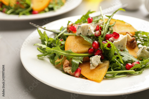 Delicious persimmon salad with pomegranate and arugula served on light grey table, closeup