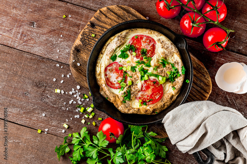  Homemade omelet with tomatoes and herbs in a pan on a wooden background, top view