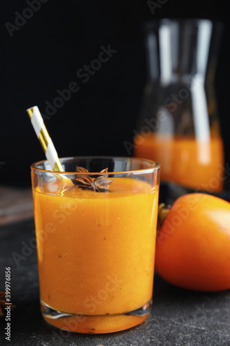 Tasty persimmon smoothie with anise and straw on black table