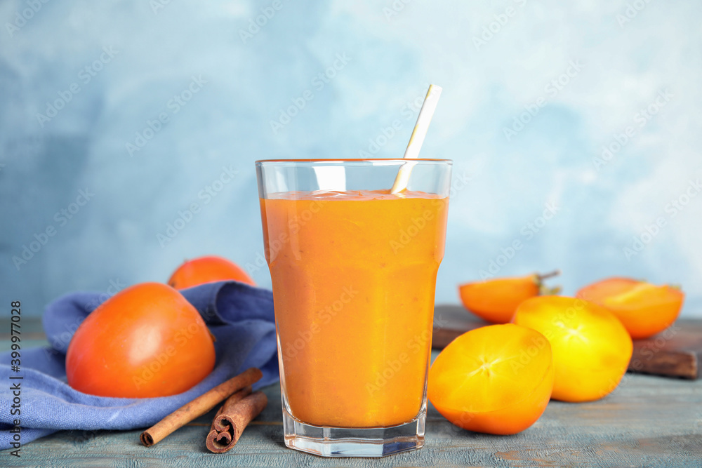 Tasty persimmon smoothie with straw and cinnamon on wooden table against light blue background Tasty persimmon smoothie with straw and cinnamon on wooden table against light blue background