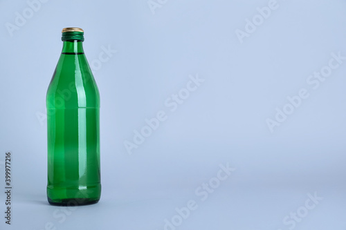 Glass bottle with water on light grey background, space for text