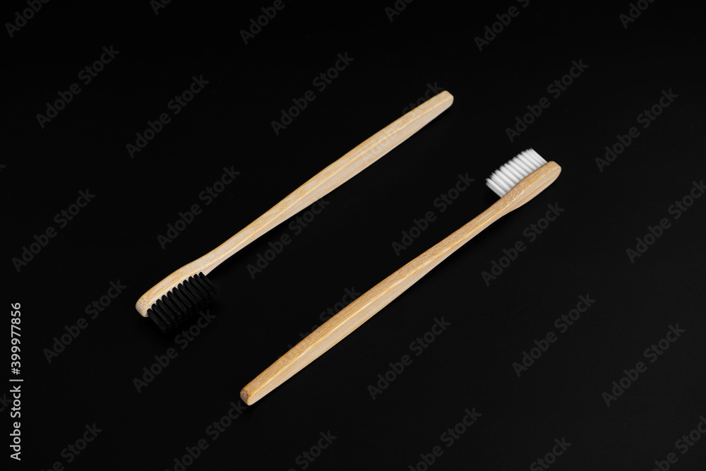Two Eco-friendly antibacterial bamboo wood toothbrushes with white and black bristles on a black background. Taking care of the environment is trending. Tolerance. Copy space Two Eco-friendly antibacterial bamboo wood toothbrushes with white and black bristles on a black background. Taking care of the environment is trending. Tolerance. Copy space