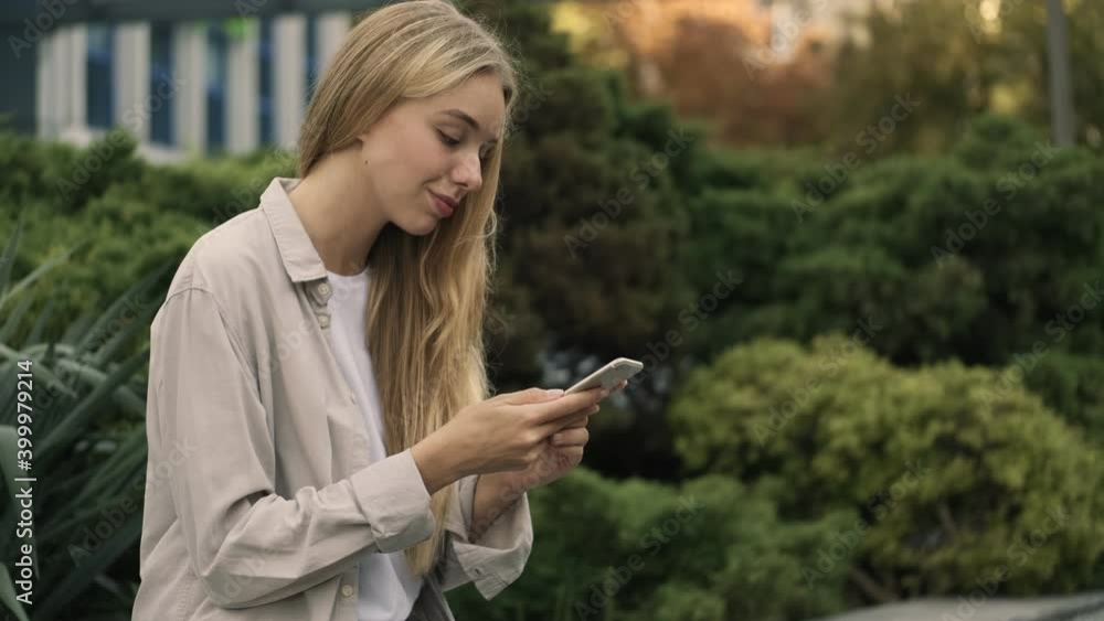 A side view of an attractive young blonde woman is using her smartphone sitting outside in the street A side view of an attractive young blonde woman is using her smartphone sitting outside in the street
