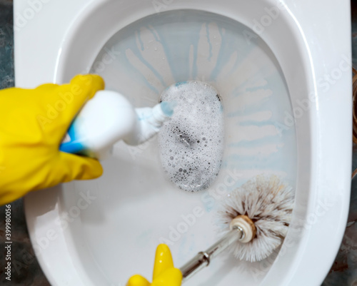 Female hand in a yellow rubber glove cleans the toilet bowl with a brush and means