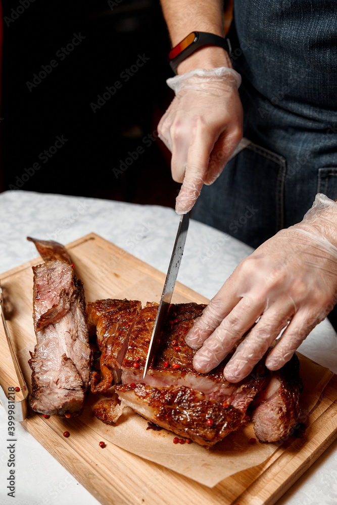Waiter with gloves cuts Tomahawk steak on a beef bone into pieces for restaurant guests. Close-up of hands