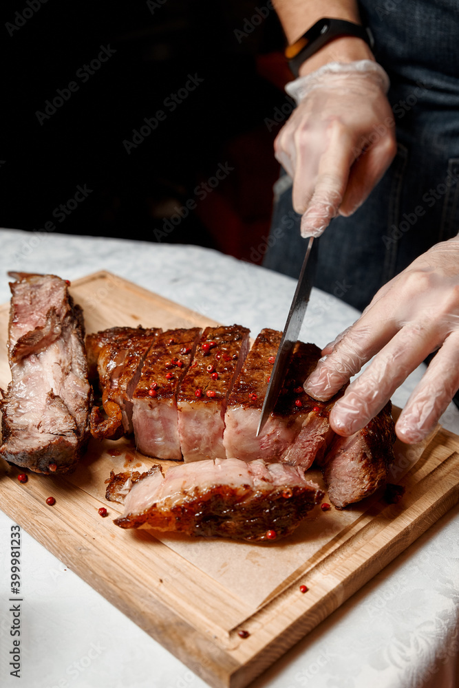 Waiter with gloves cuts Tomahawk steak on a beef bone into pieces for restaurant guests. Close-up of hands