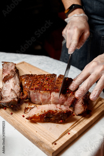 Waiter with gloves cuts Tomahawk steak on a beef bone into pieces for restaurant guests. Close-up of hands