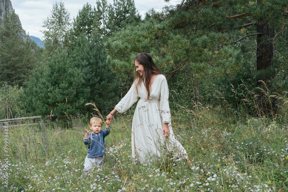 Fototapeta premium Young mother wearing white dress walking and enjoying with little kid boy in pine mountain forest
