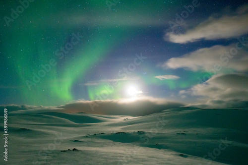 Snowy landscape lit by moon in the starry sky during the Northern Lights (Aurora Borealis), Skarsvag, Nordkapp, Troms og Finnmark photo