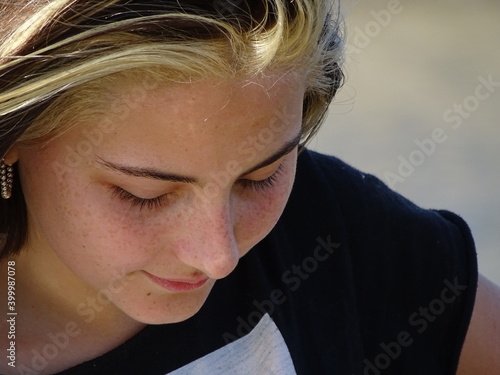 retrato rostro chica adolescente blanca con cabello castaño claro con mechones blancos con remera negra mirando hacia abajo, en un dia soleado photo
