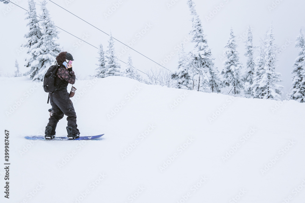 Snowboarder female riding on winter snow cowered slop on snowboard and talking on mobile phone