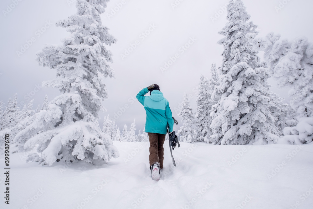 Snowboarder female walking through the forest carrying snowboard. Powder Day. Walking throw deep snow, snowboarder on winter holiday