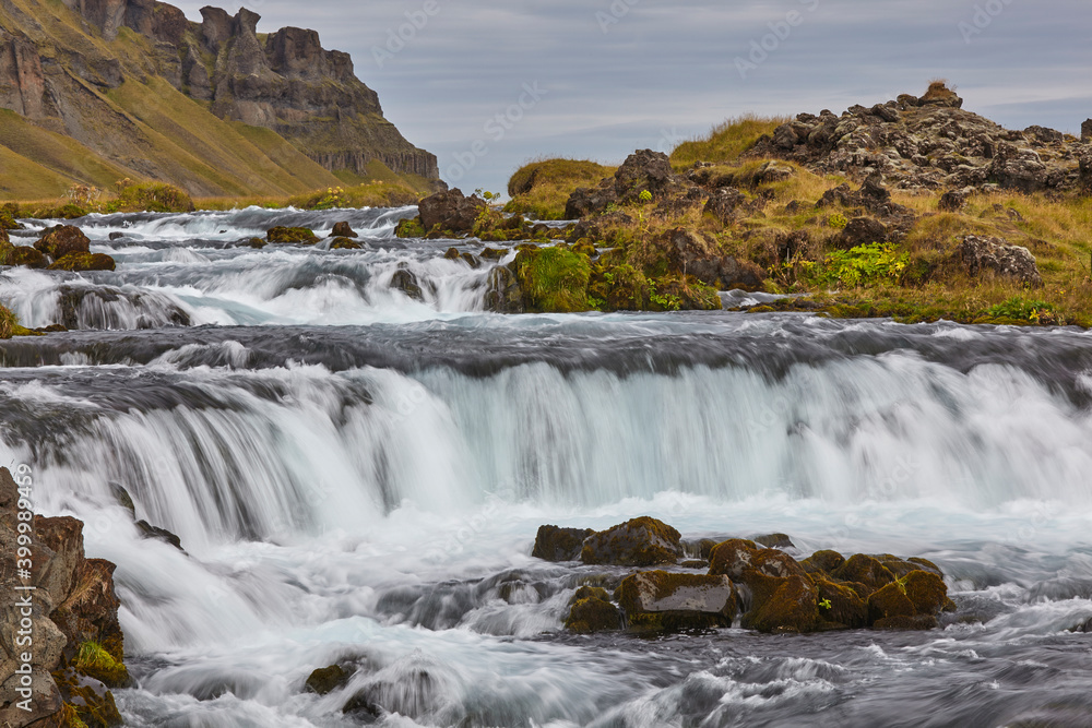 A classic Icelandic landscape, a river flowing along the base of a ...
