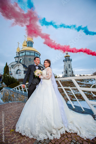 the groom and the bride stand in front of the church in colorful smoke