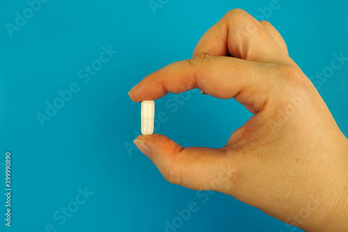 the right female hand holds a white oval probiotic capsule on a blue background . medicines