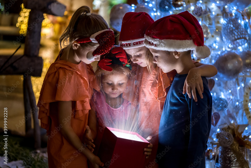 Little happy children looking inside of magic gift box standing by Christmas tree. Merry Christmas and happy holidays